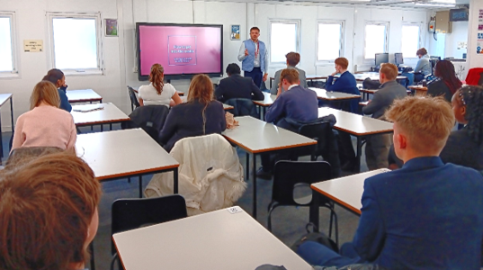 A person standing in front of a group of people in a classroom

Description automatically generated